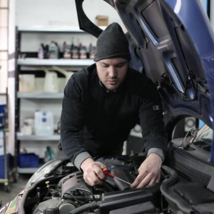 A man working on the hood of his car.